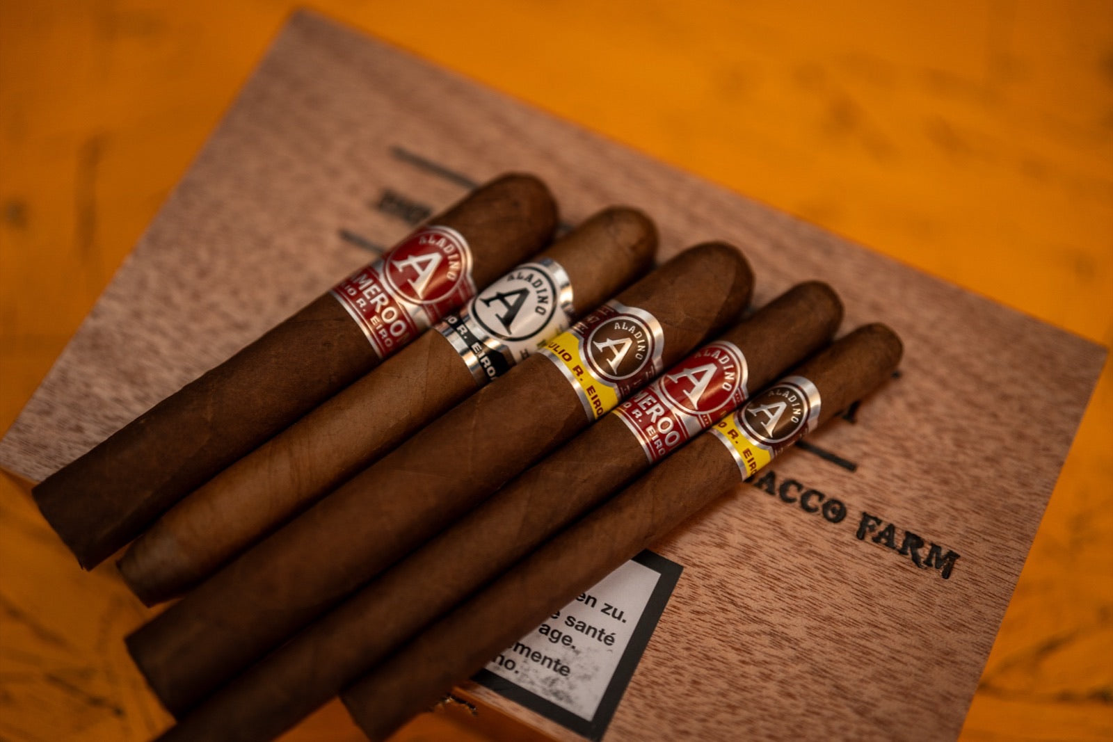 A fan of Aladino cigars including Corojo Reserva and Maduro with branded bands on a wooden tobacco farm box