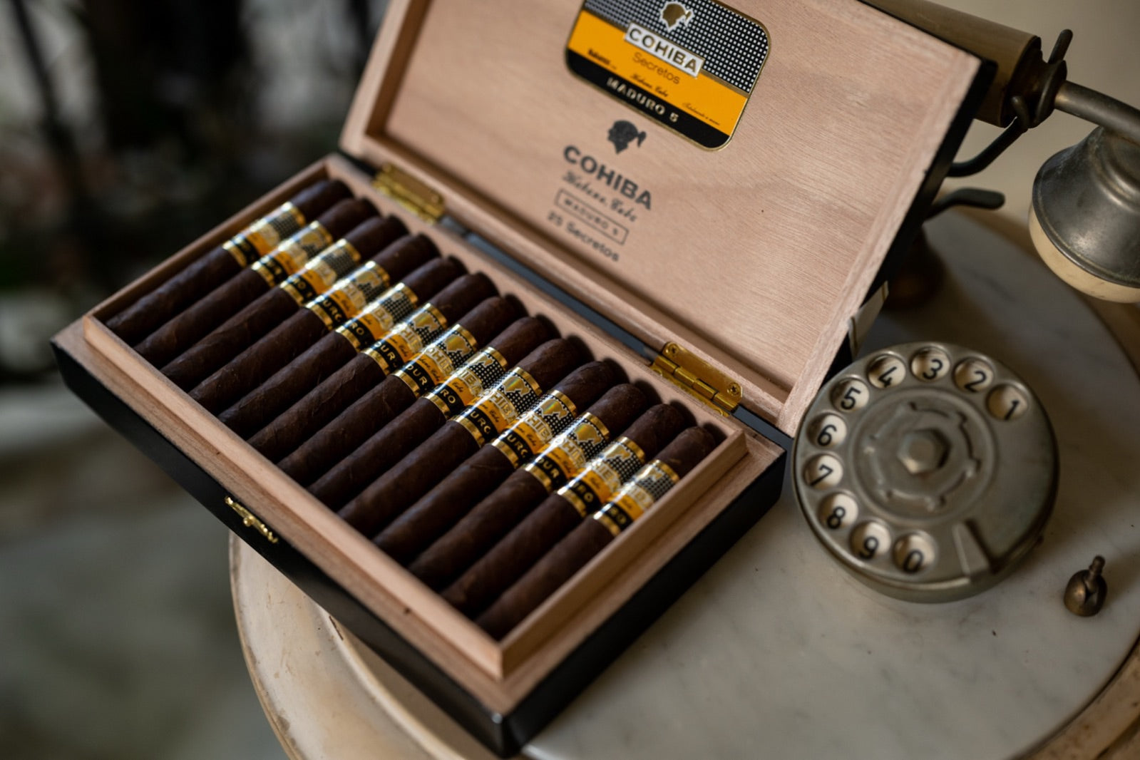 Open box of Cohiba cigars beside a vintage rotary phone, the best cigar gift for your dad