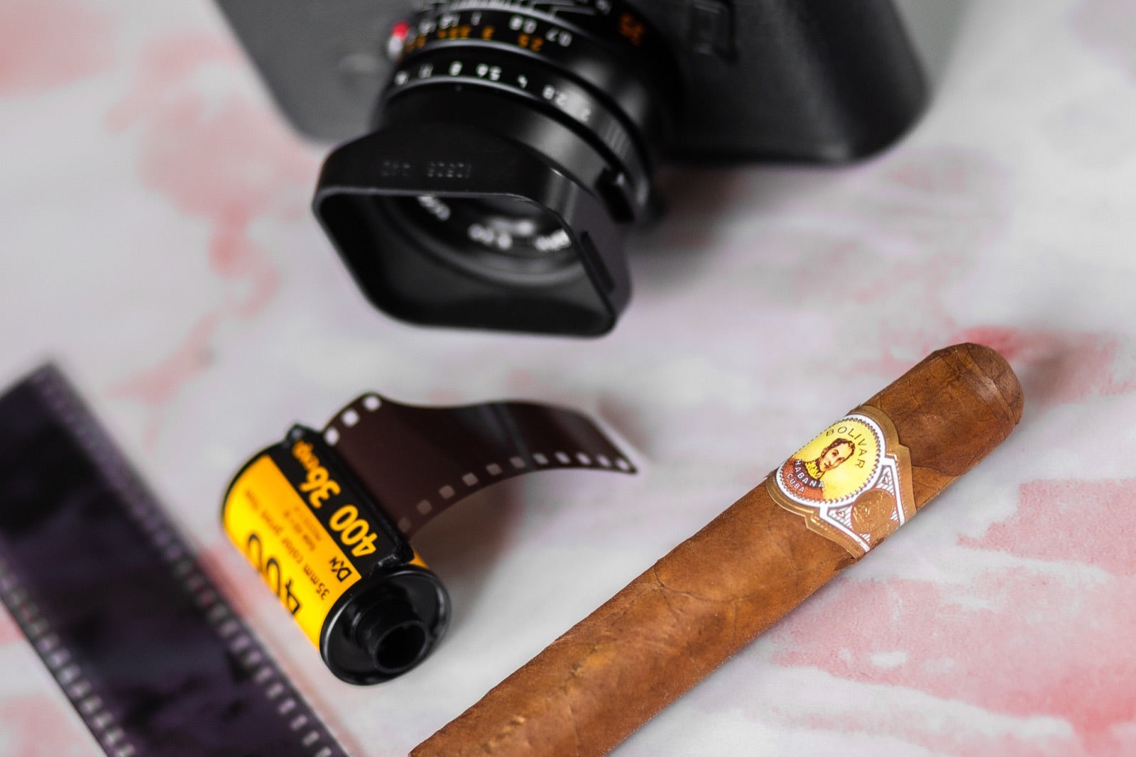 A premium Cuban cigar beside a film camera on marble, a stylish cigar gift for a husband
