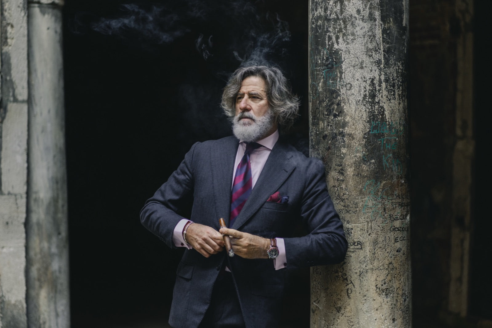 Distinguished gentleman in a tailored suit enjoying one of the best cigars for golf, smoke rising against a weathered stone column