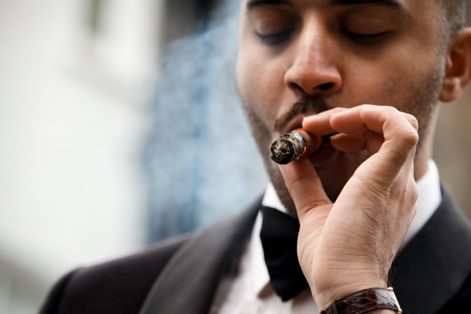 Elegant man in black-tie tuxedo lighting one of the best cigars for special occasions, soft smoke rising