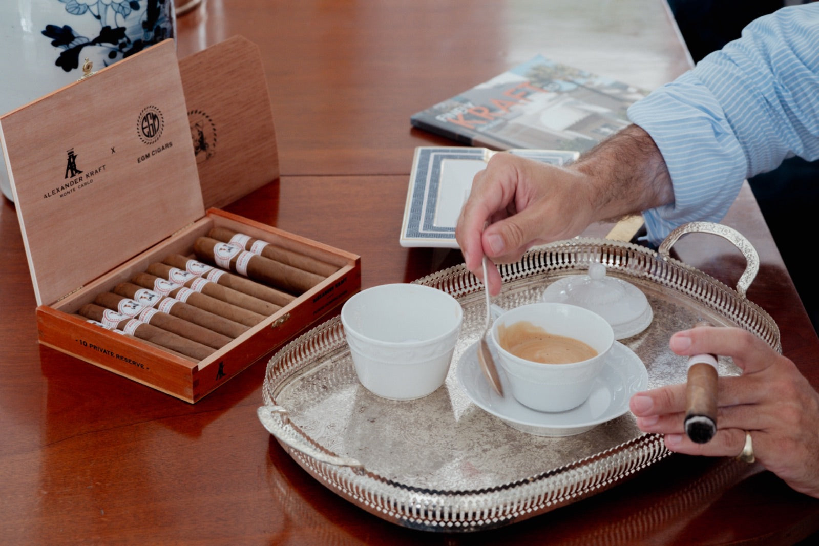 Open box of premium Cuban cigars beside a lit cigar in hand and espresso on a silver tray, best Cuban cigars 2026