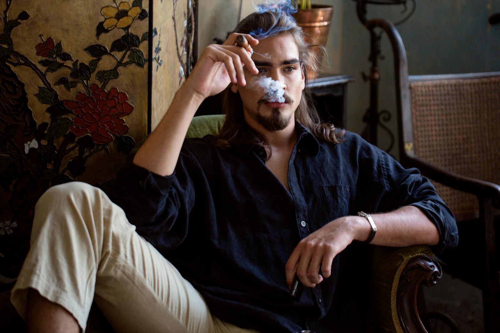 Man relaxing in a vintage lounge armchair enjoying one of the best Cuban cigars for beginners amid soft smoke