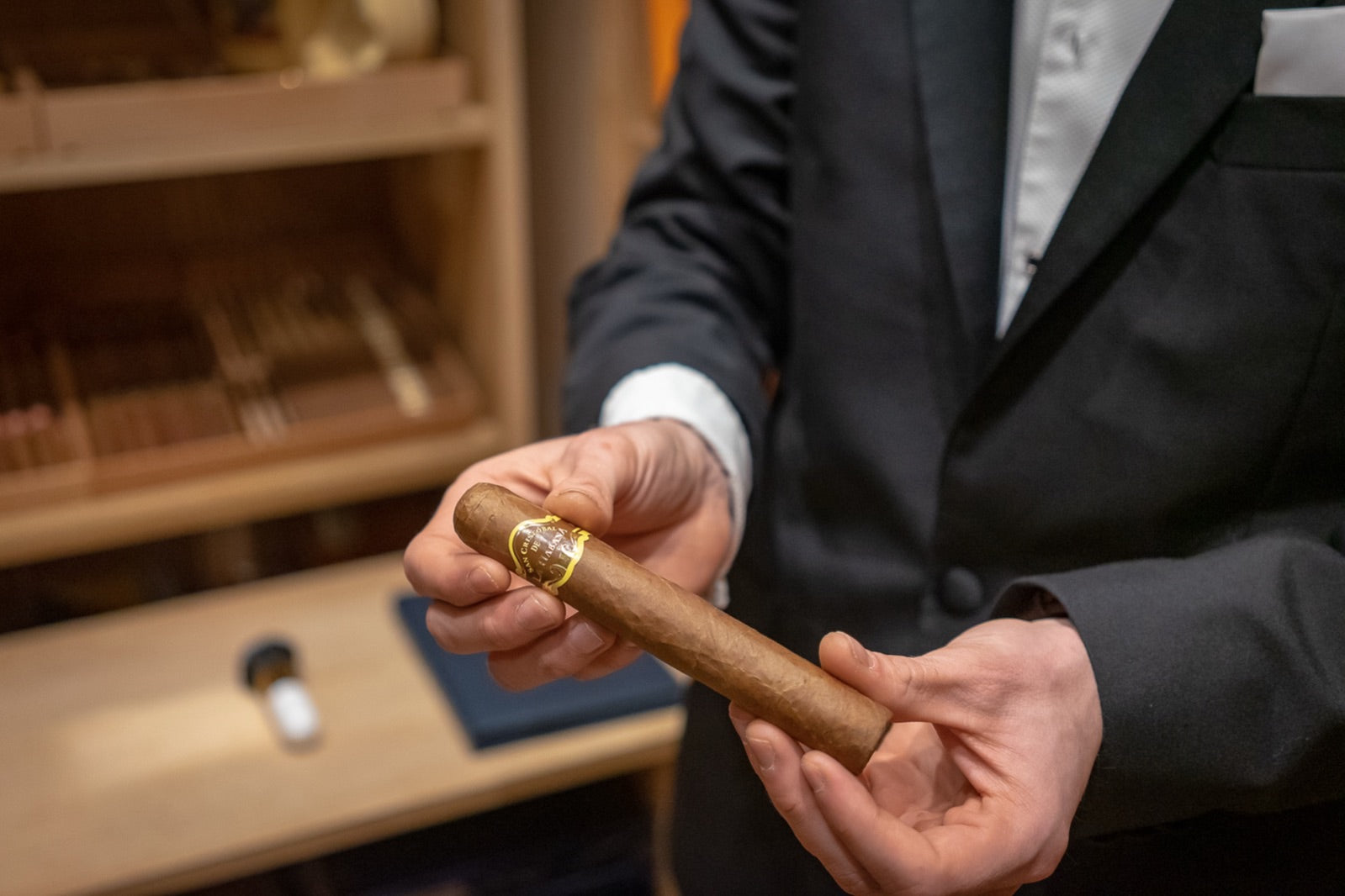 Tuxedoed connoisseur presenting a premium maduro cigar by an open humidor in a refined cigar lounge