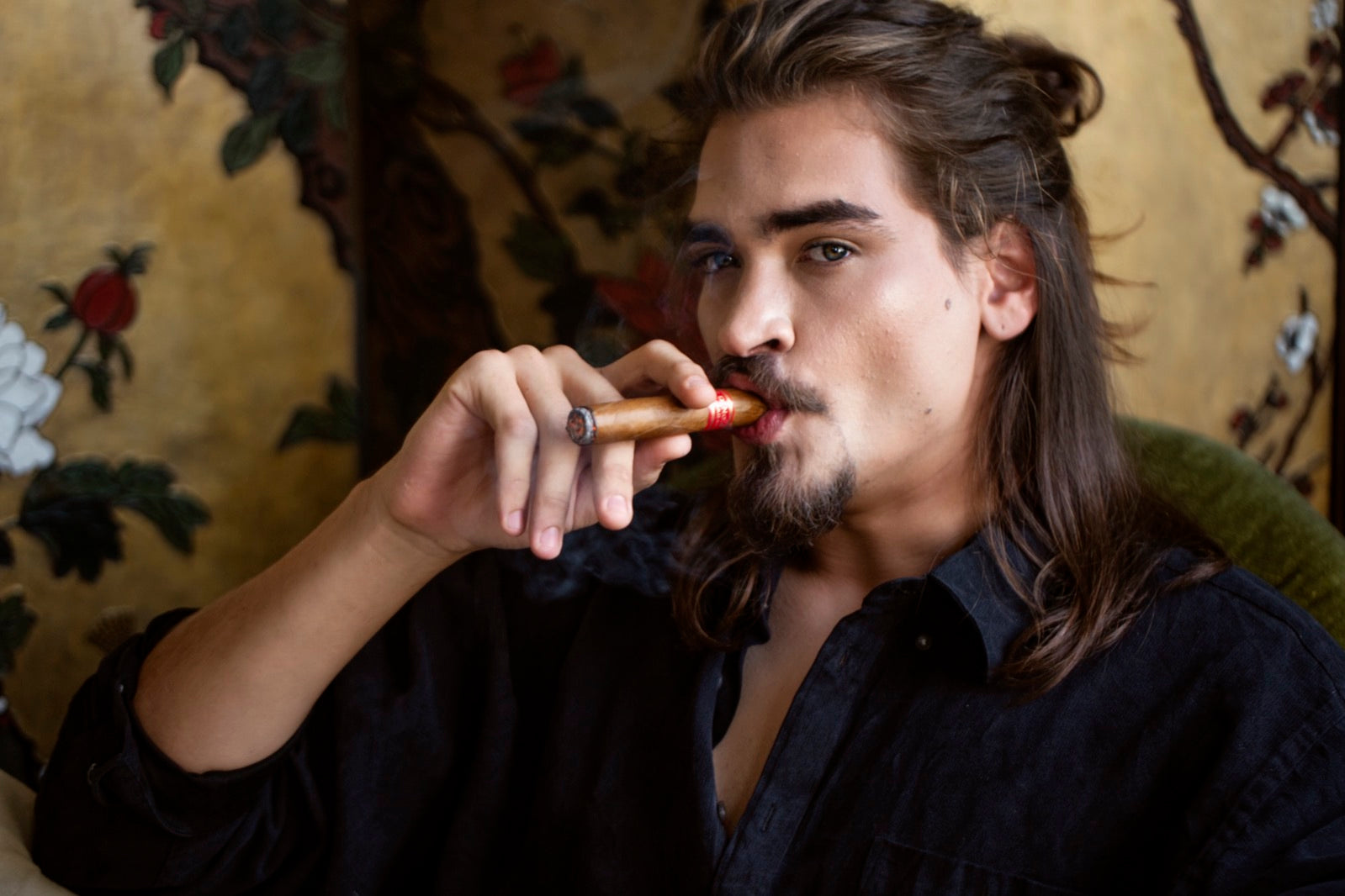 Gentleman lighting one of the best short smoke cigars in a richly lit lounge with an ornate gold floral backdrop
