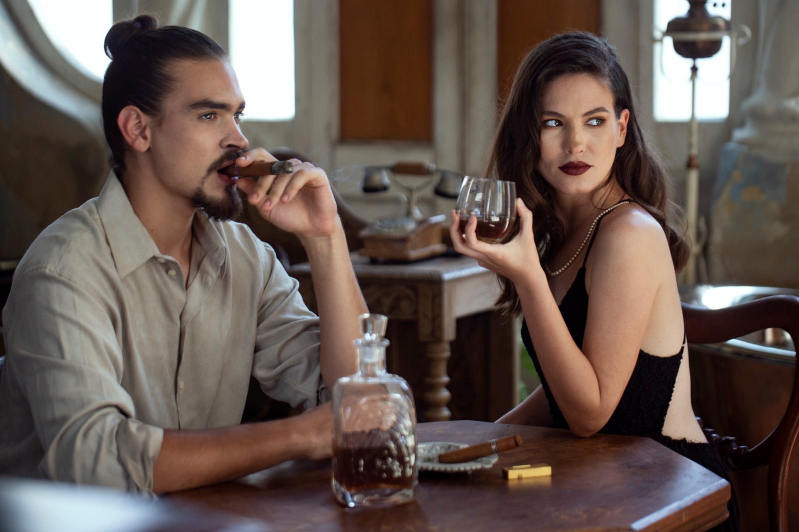 Man smoking a cigar at a lounge table with a glass of spirits, ashtray and decanter, illustrating cigar lounge etiquette