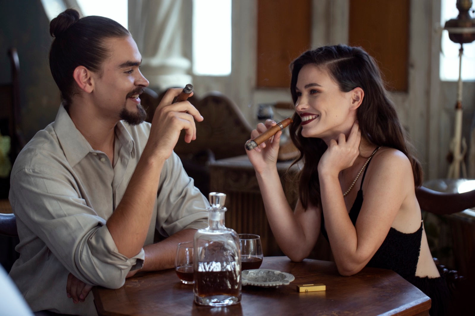 Couple relaxing in a vintage lounge sharing lit premium cigars, illustrating cigar wrappers from Connecticut to Maduro