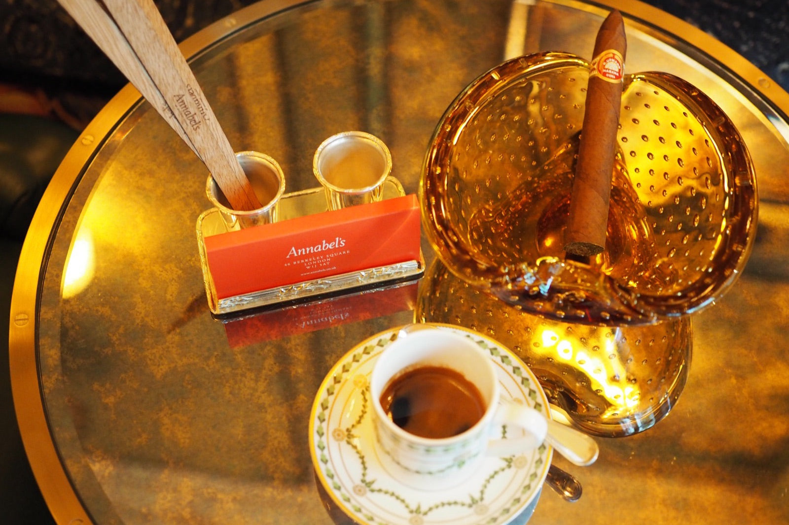 Premium cigar resting in a golden ashtray beside an espresso, set for tasting on a gilded table in an elegant lounge