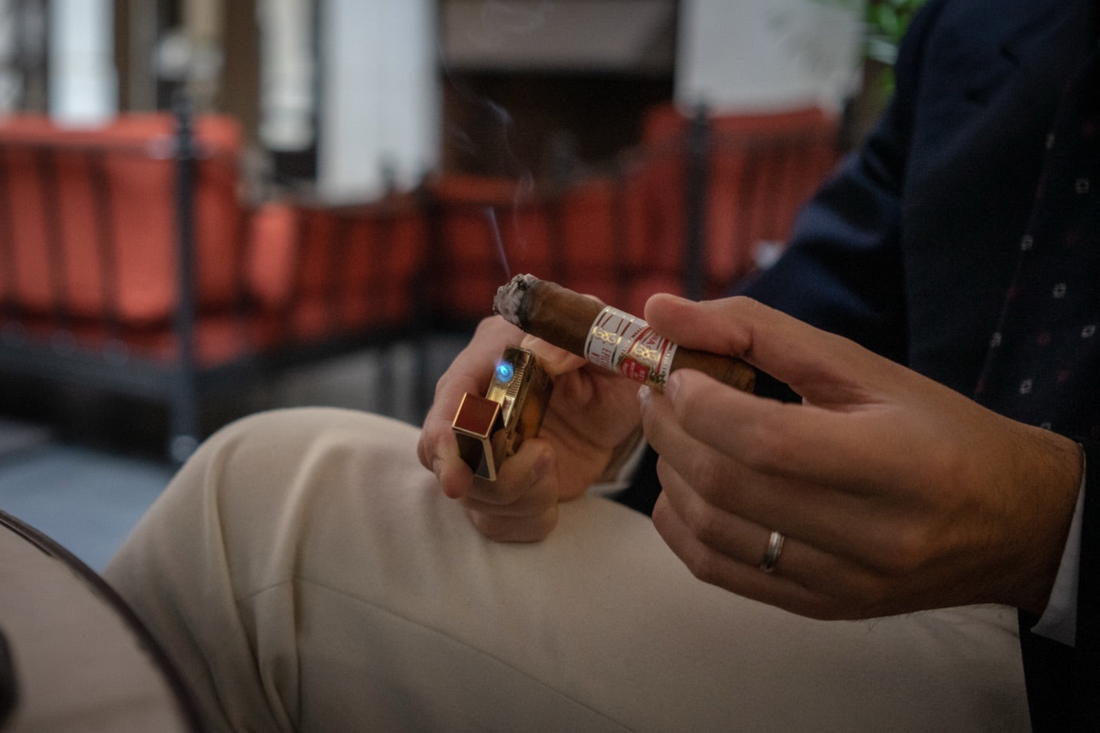 Gentleman lighting a premium cigar from a luxury cigar gift set with a gold lighter, smoke curling in an elegant lounge
