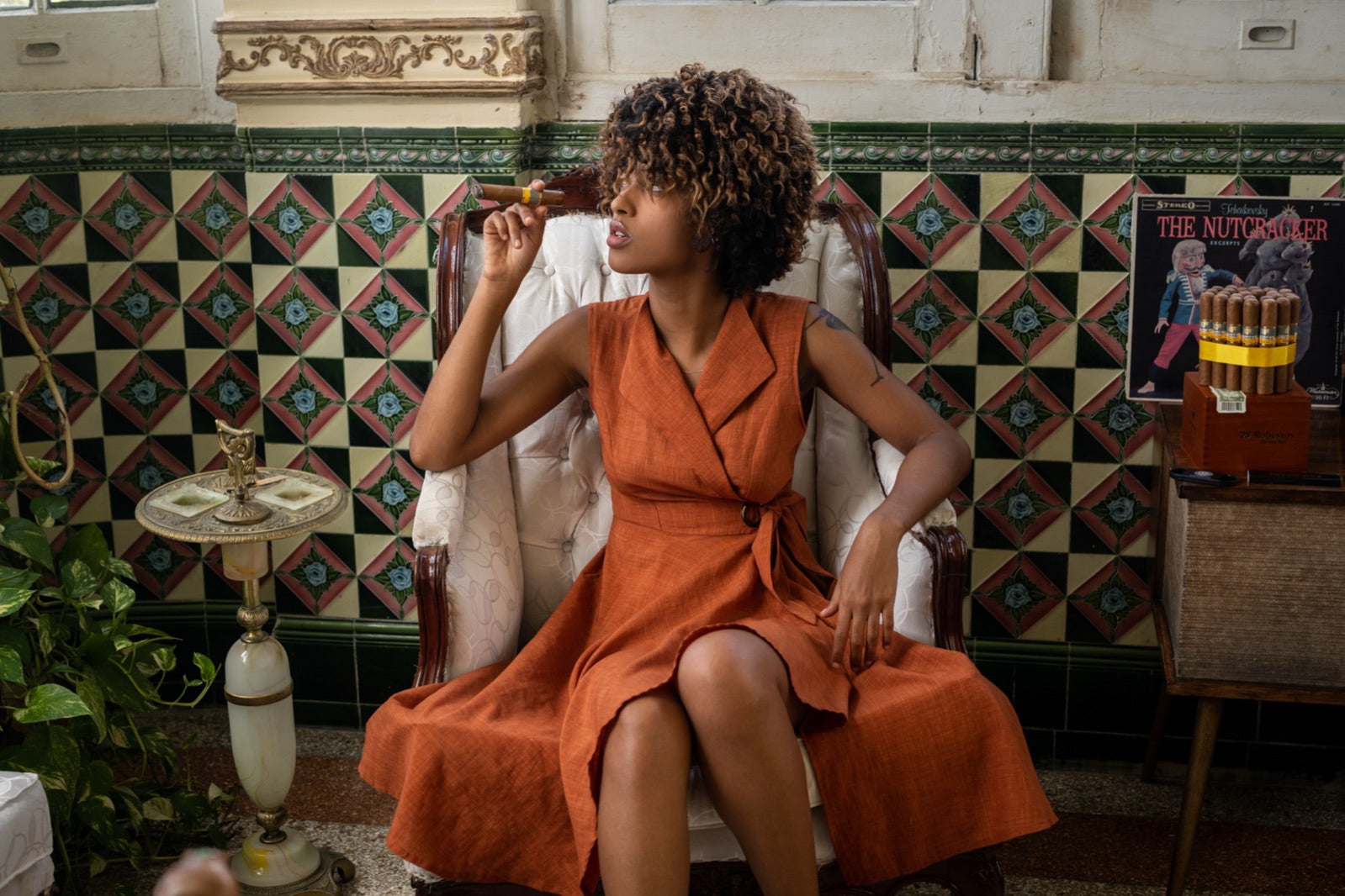 Woman relaxing in a colonial Havana armchair holding a premium cigar with a box of Oliva cigars beside her