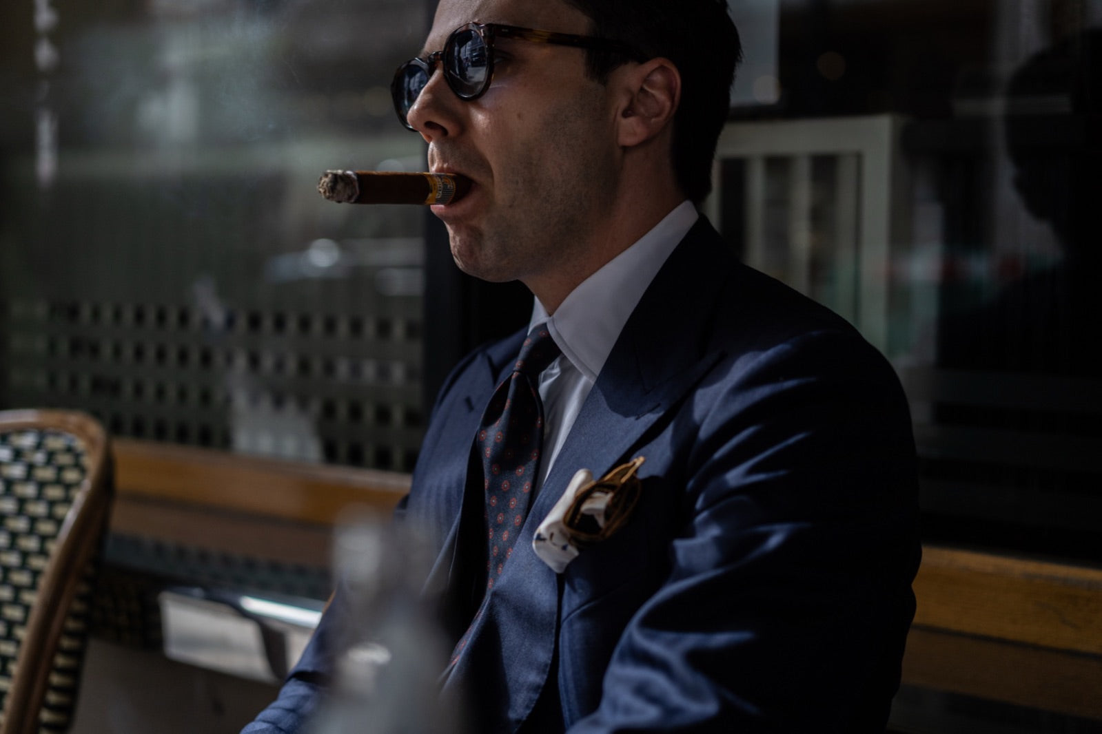 Elegant gentleman in a tailored blue suit smoking a premium Cuban cigar in a refined lounge setting