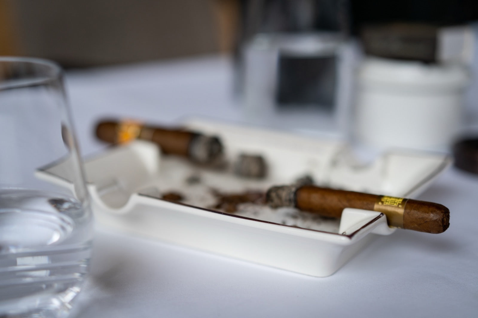 Two premium cigars resting on a white ashtray beside glasses, illustrating beginner cigar mistakes to avoid when smoking