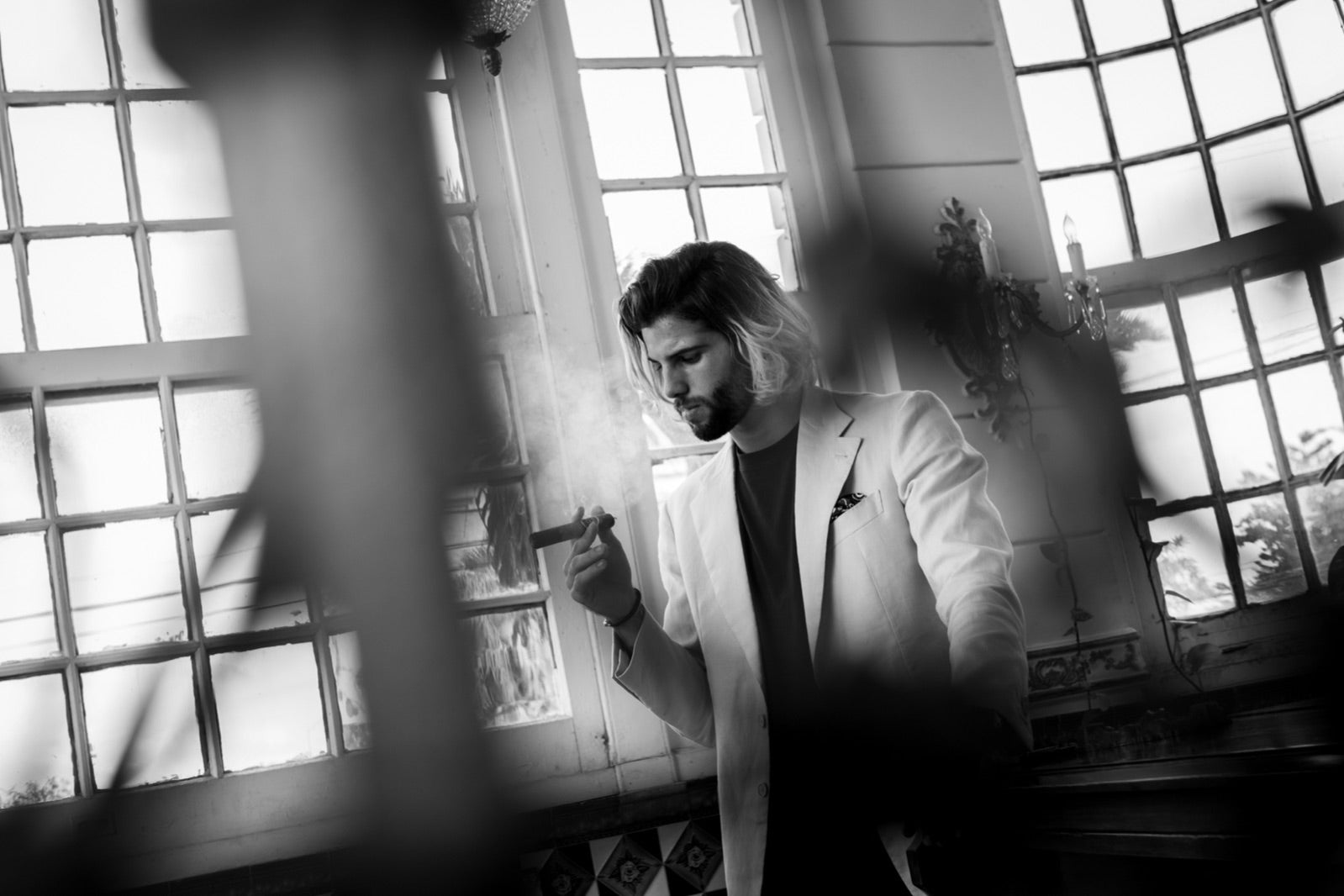 Elegantly dressed man in a tailored suit savouring a premium cigar by tall windows, the perfect cigar for an anniversary gift