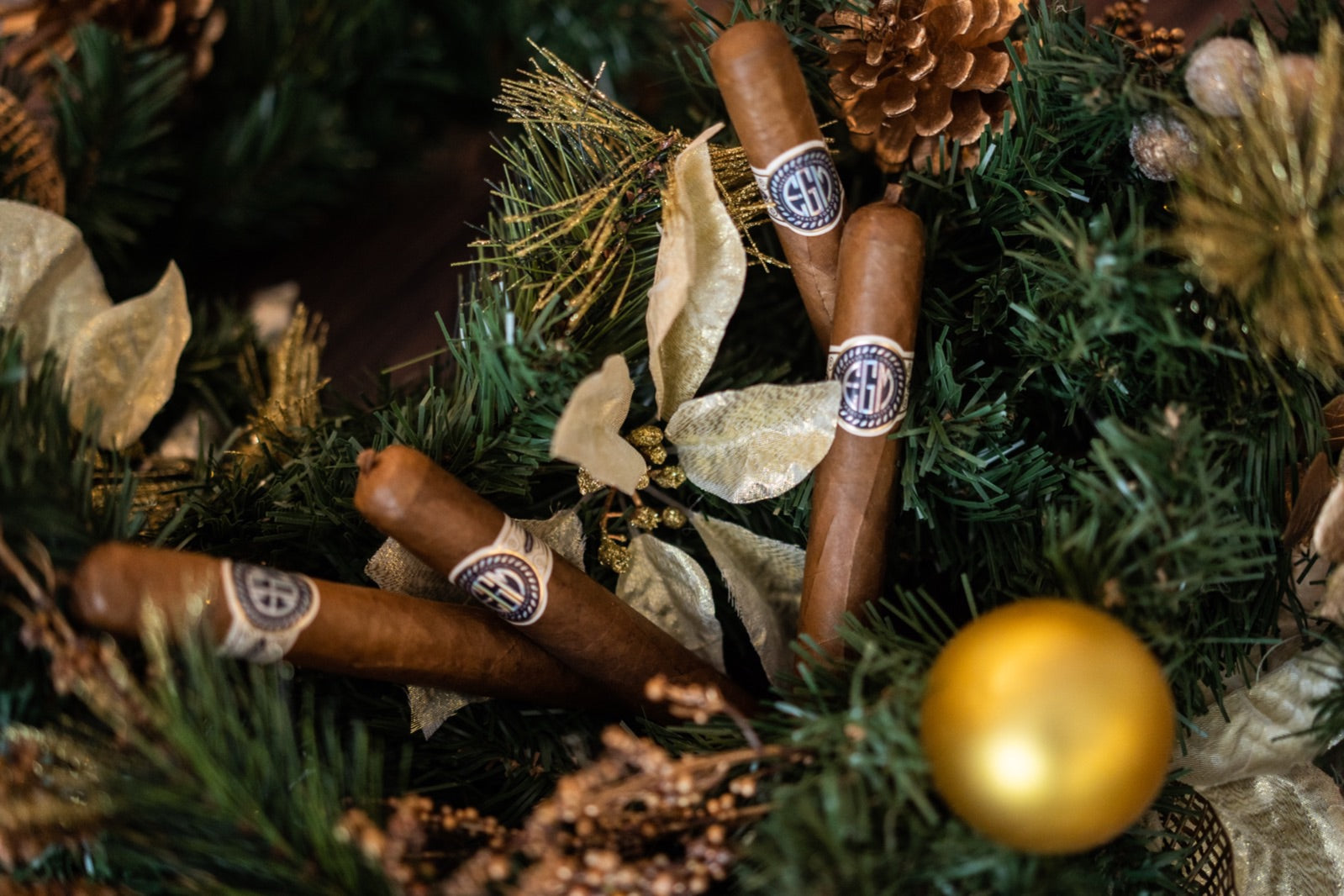 Premium cigars nestled in a gold and green Christmas wreath with pinecone and bauble, best cigars for the festive season