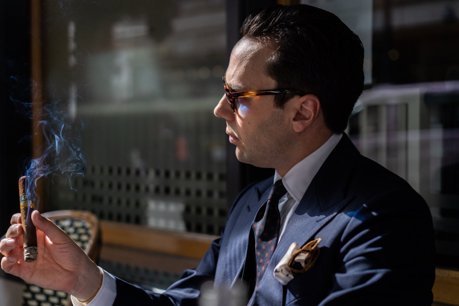 Elegant gentleman in a tailored navy suit smoking one of the best cigars for a wedding in a sunlit bar