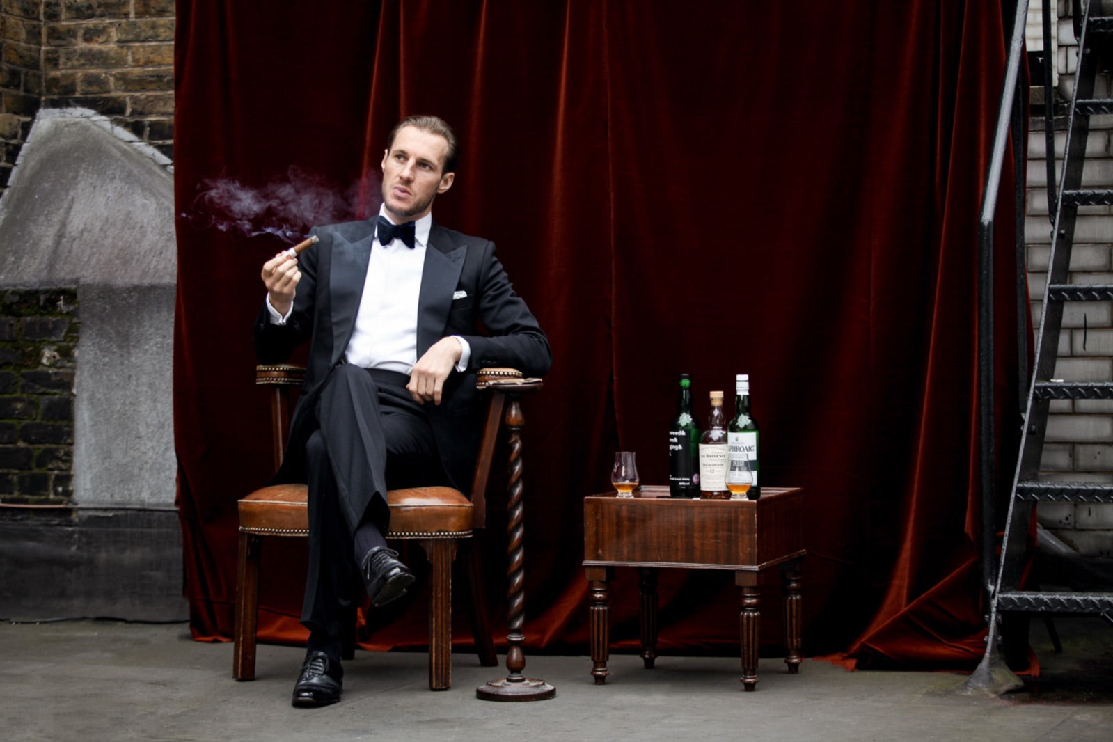 Man in black tie enjoying one of the best cigars to give as a gift in a velvet lounge with whisky