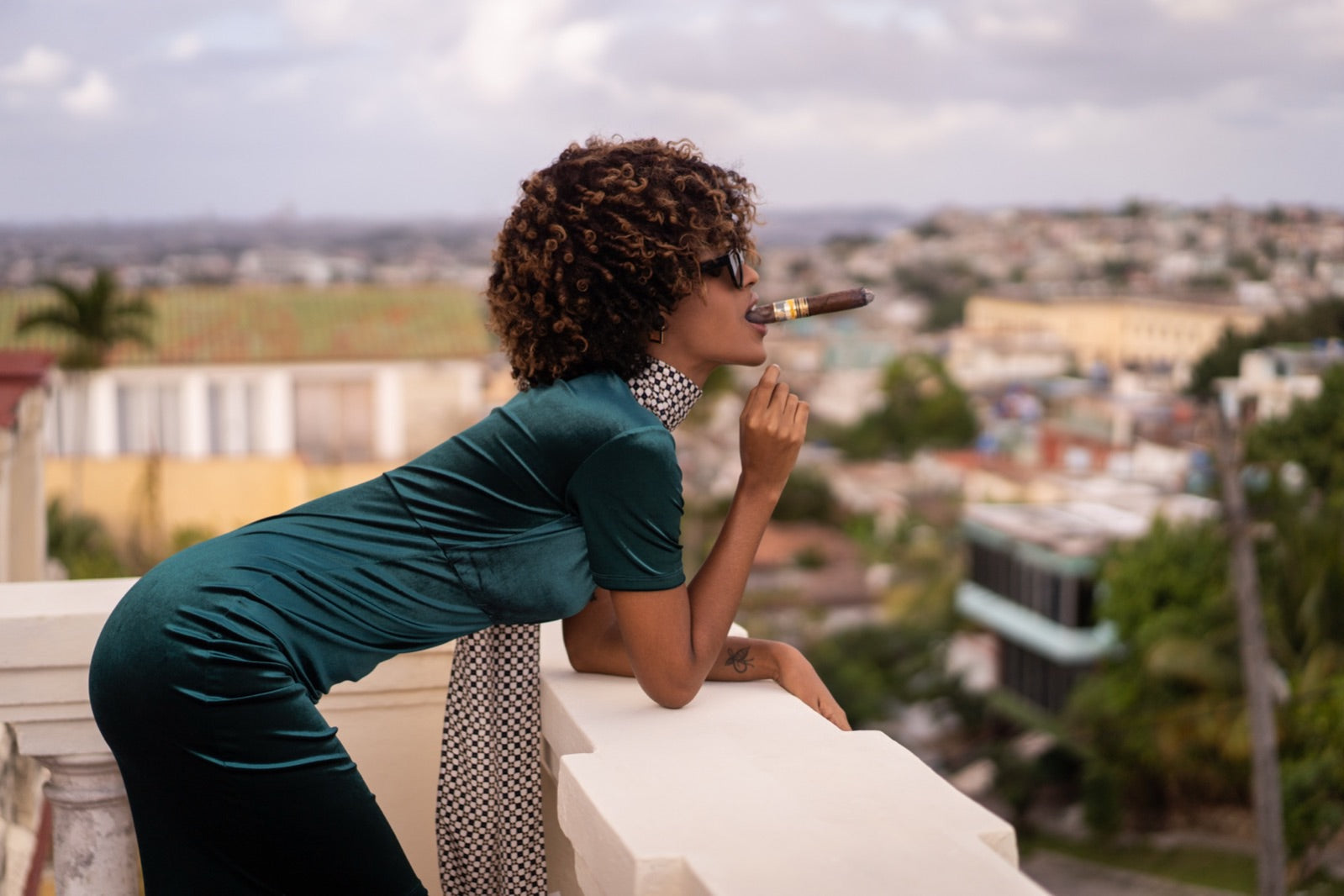 Elegant woman smoking a premium cigar on a rooftop terrace overlooking the city skyline, best Connecticut cigars editorial