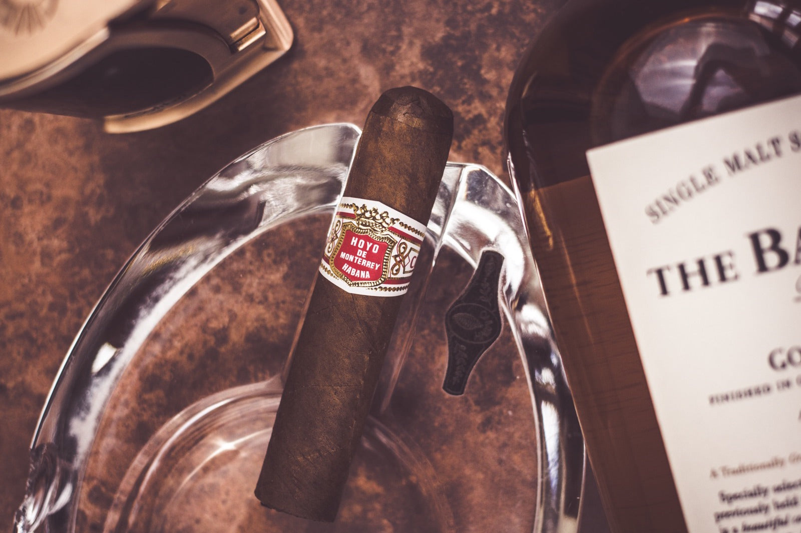 Full-bodied Hoyo de Monterrey cigar standing in a crystal ashtray beside a single malt whisky bottle and cutter