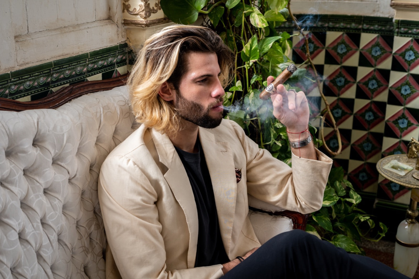 Man in cream jacket savouring one of the best medium-bodied cigars, slow curl of smoke rising in an ornate tiled Havana lounge