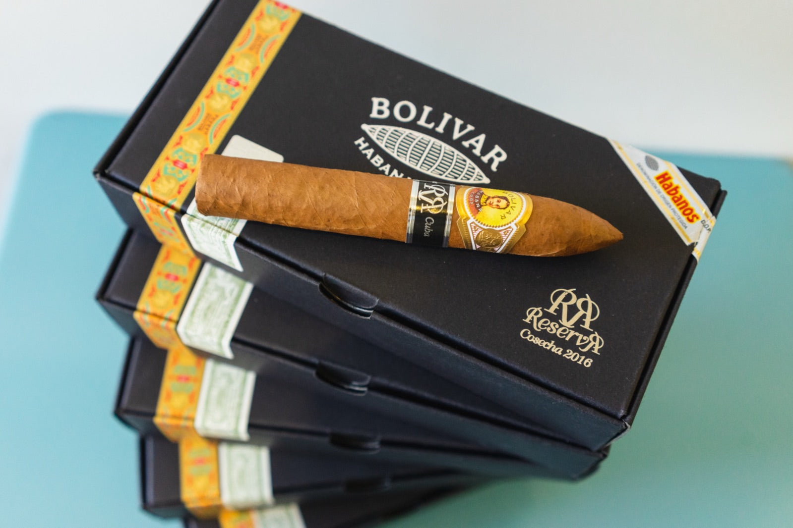 Single Bolivar Belicosos Finos Cuban cigar resting on a stack of black Bolivar Reserva Habanos boxes