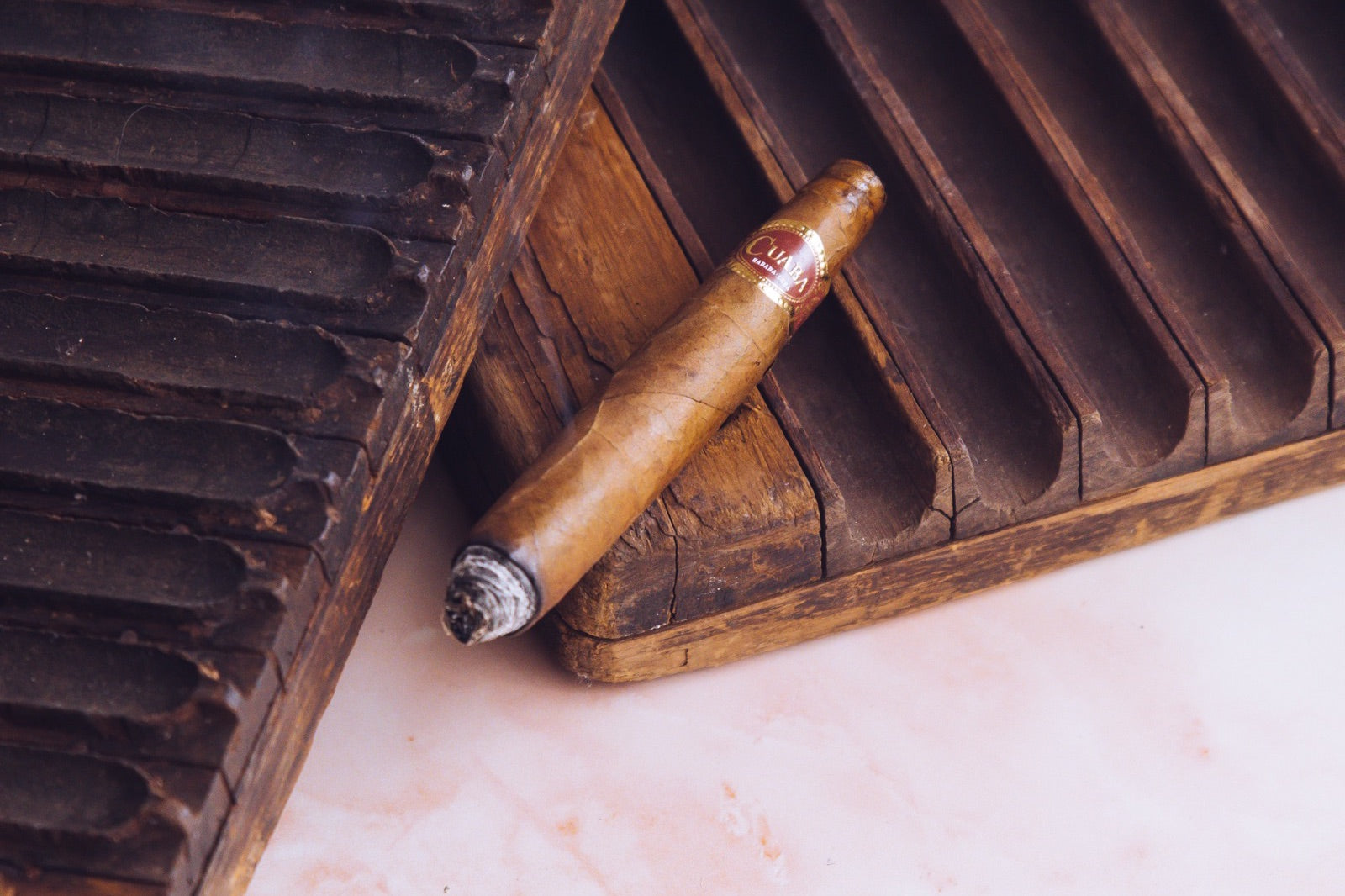 A single lightly lit Cuban corona cigar resting on a rustic wooden cigar mould, illustrating the Corona vs Petit Corona format comparison