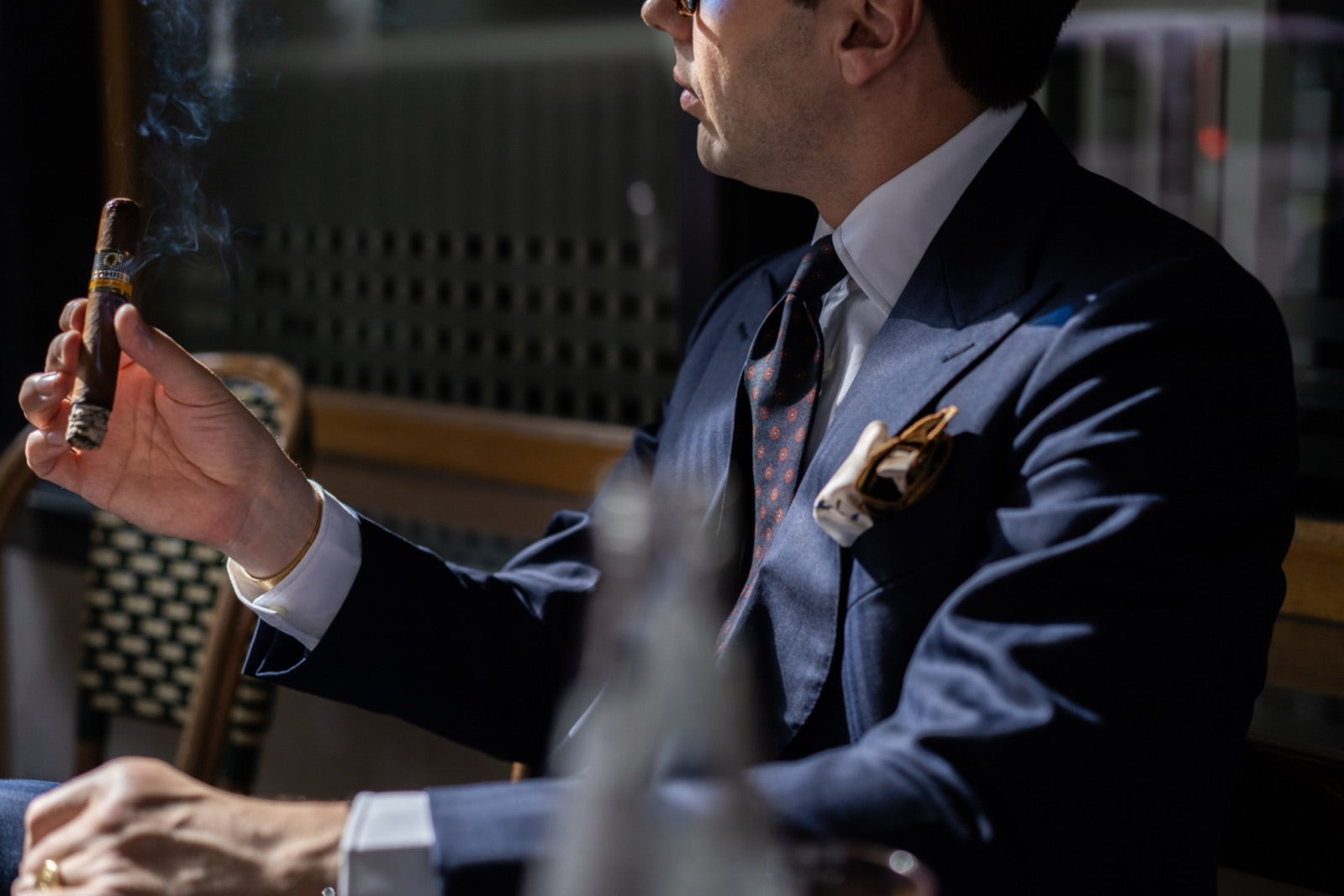 Elegant man in a tailored navy suit enjoying a premium cigar in a sunlit lounge, illustrating how to buy cigars as a gift