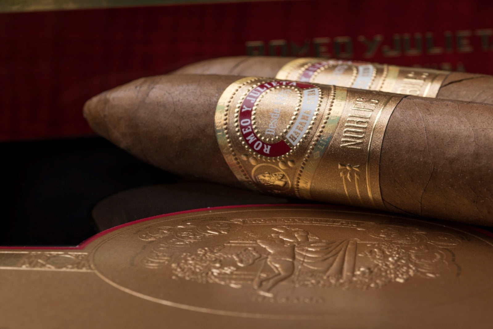 Romeo y Julieta Linea de Oro cigar resting on a red lacquered box with gold medallion, a luxury Cuban cigar close-up