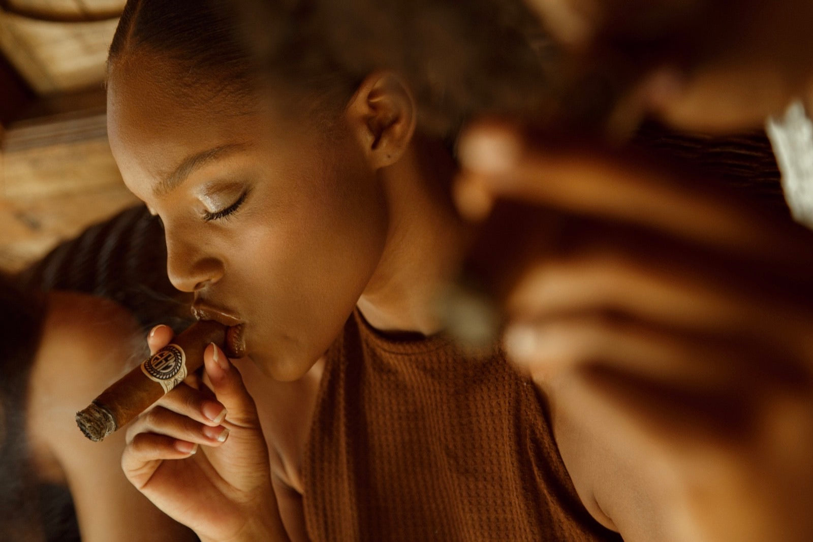 Woman lighting a premium cigar in warm low light inside a rustic interior